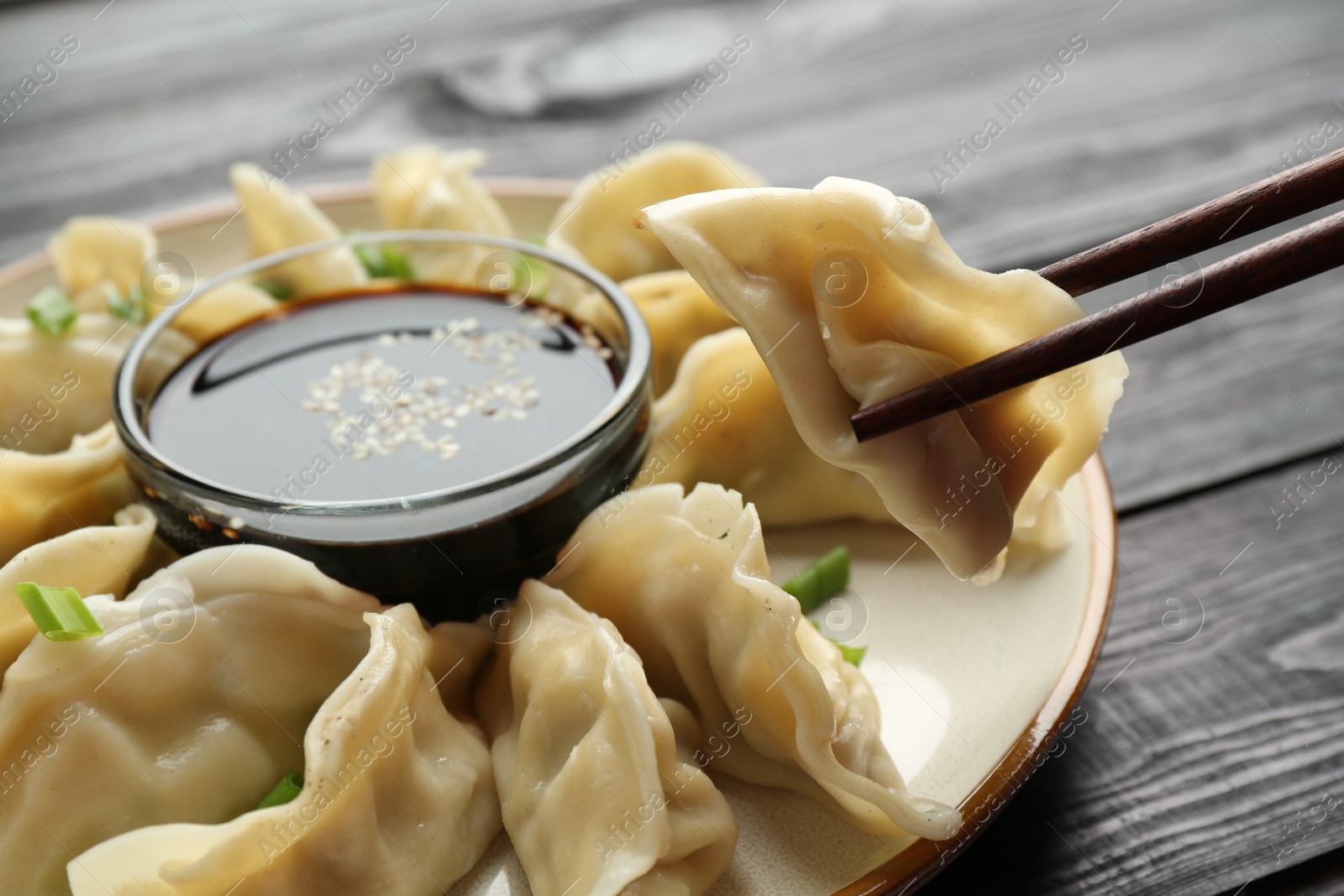 Photo of Taking tasty boiled gyoza (dumpling) with chopsticks at black wooden table, closeup