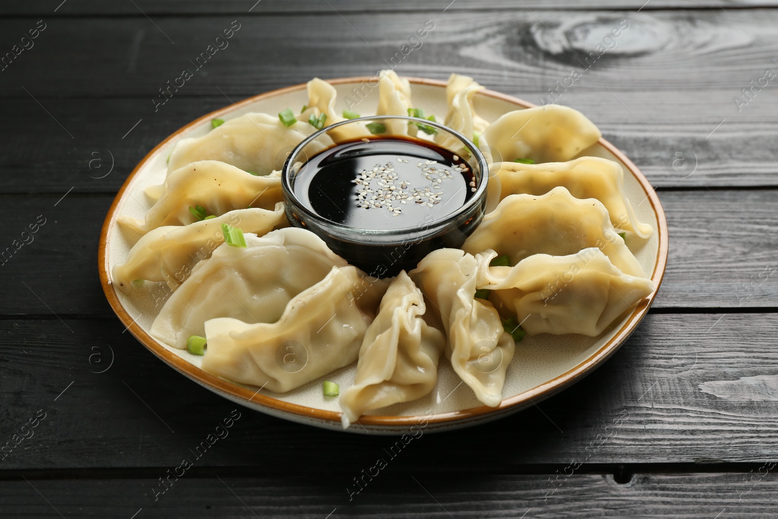 Photo of Tasty boiled gyoza (dumplings) with green onion and soy sauce on black wooden table