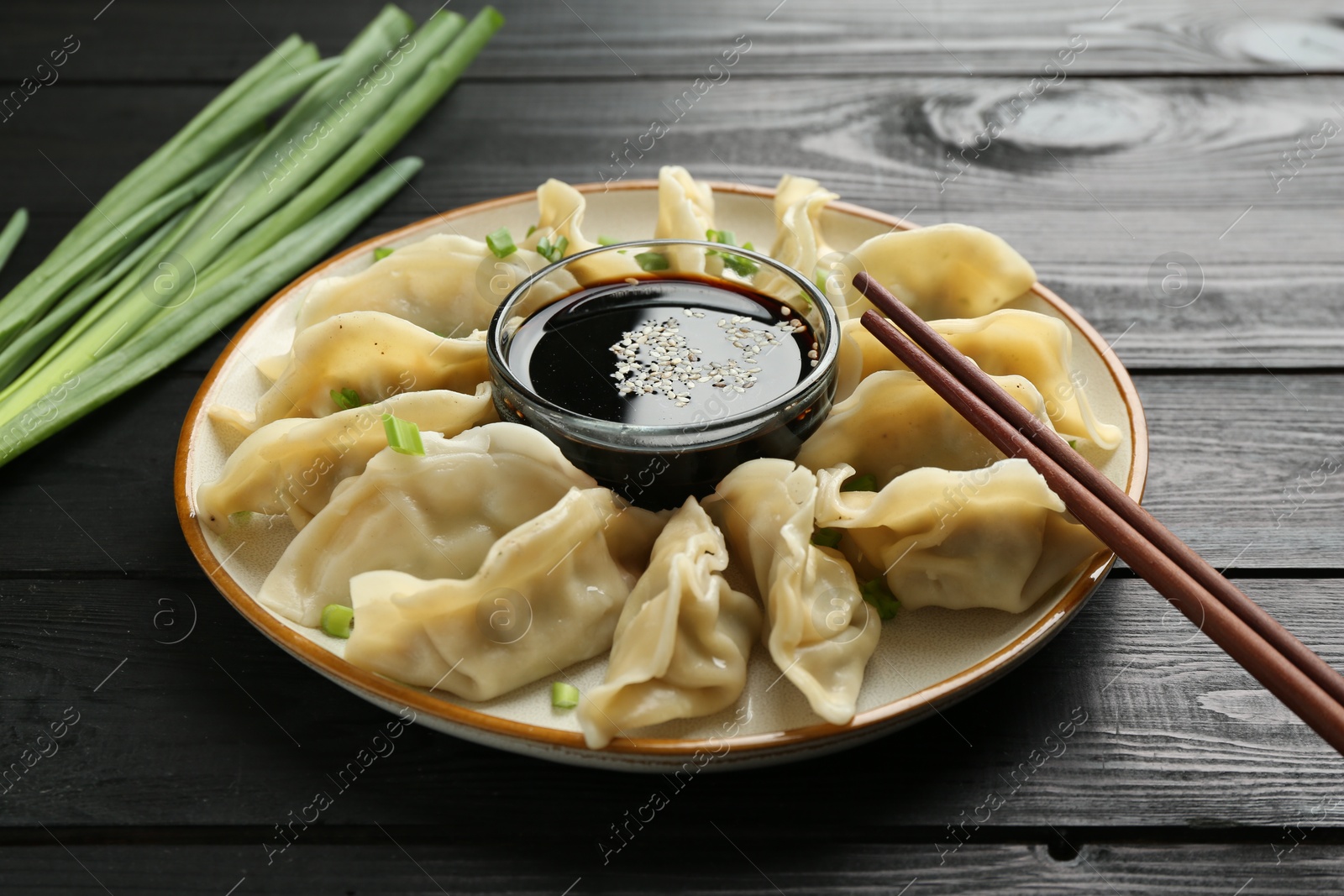 Photo of Tasty boiled gyoza (dumplings) with green onion served on black wooden table, closeup