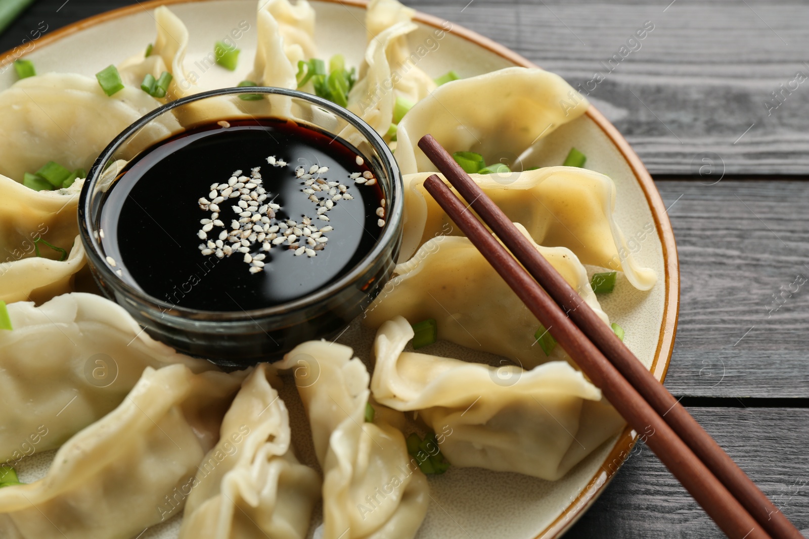 Photo of Tasty boiled gyoza (dumplings) with green onion served on black wooden table, closeup