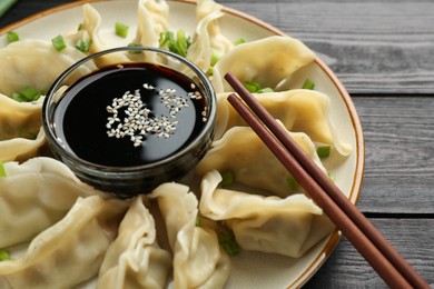 Photo of Tasty boiled gyoza (dumplings) with green onion served on black wooden table, closeup