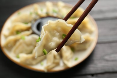 Photo of Chopsticks with tasty boiled gyoza (dumpling) over table, closeup