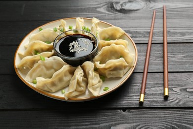 Photo of Tasty boiled gyoza (dumplings) with green onion served on black wooden table