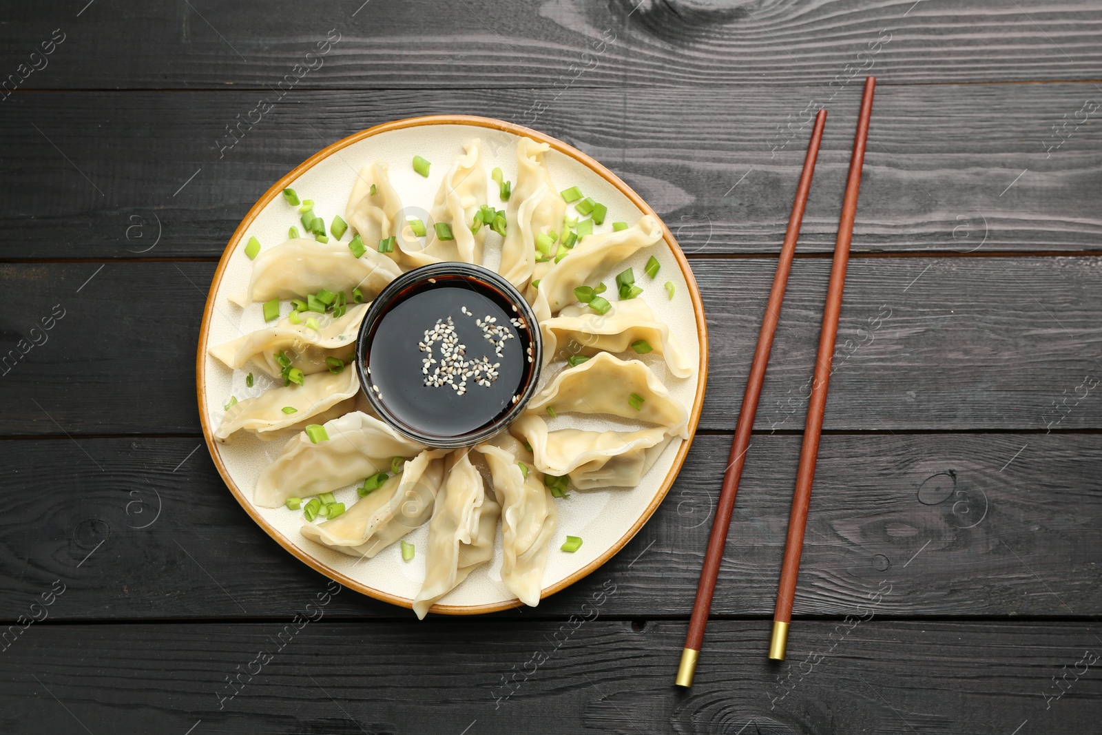 Photo of Tasty boiled gyoza (dumplings) with green onion served on black wooden table, flat lay