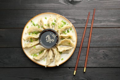 Photo of Tasty boiled gyoza (dumplings) with green onion served on black wooden table, flat lay