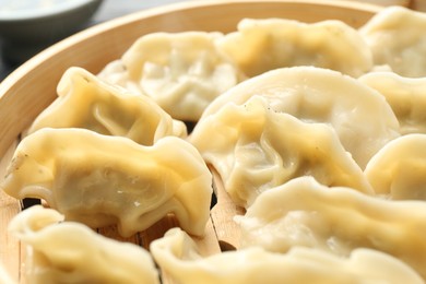 Photo of Tasty boiled gyoza (dumplings) in bamboo steamer on table, closeup