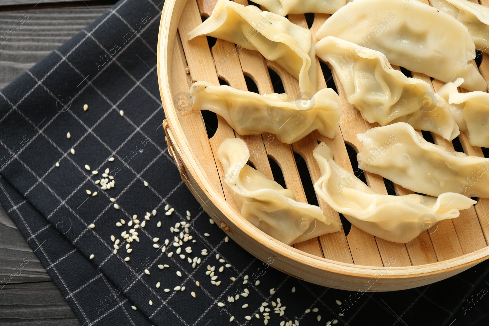 Photo of Tasty boiled gyoza (dumplings) with sesame on black wooden table, top view