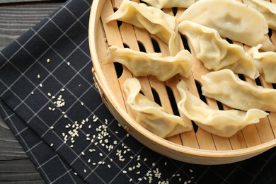 Photo of Tasty boiled gyoza (dumplings) with sesame on black wooden table, top view