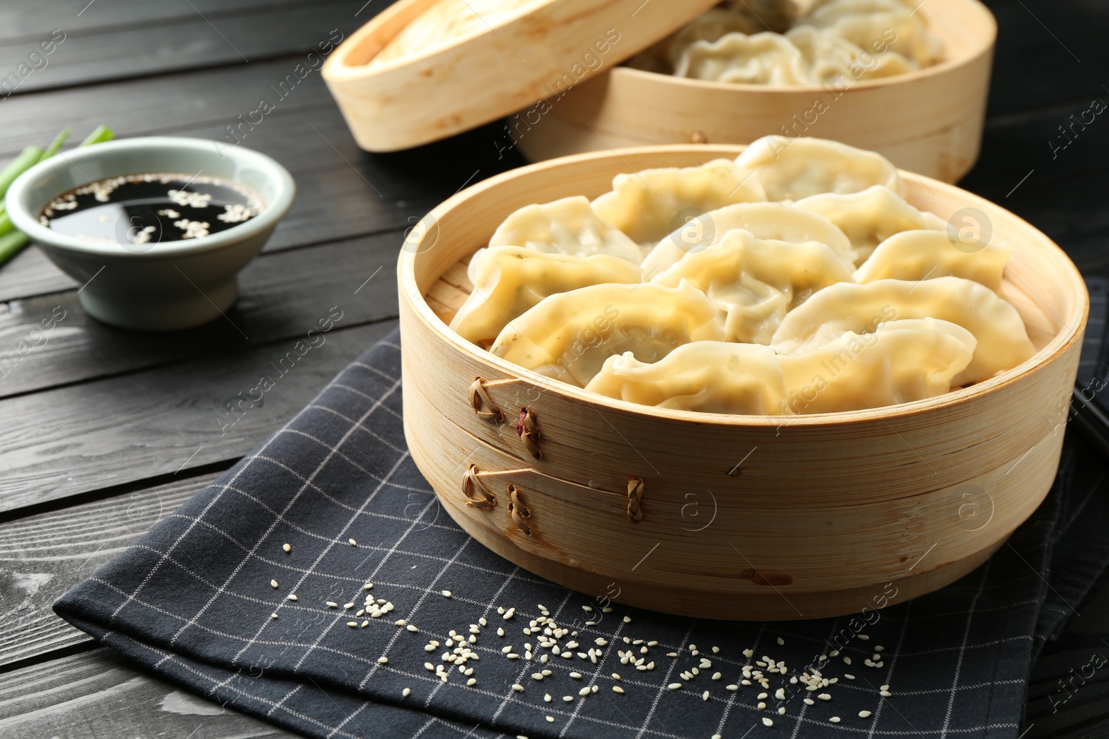 Photo of Tasty boiled gyoza (dumplings) with soy sauce and sesame on black wooden table