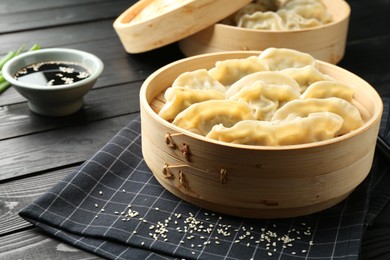 Photo of Tasty boiled gyoza (dumplings) with soy sauce and sesame on black wooden table