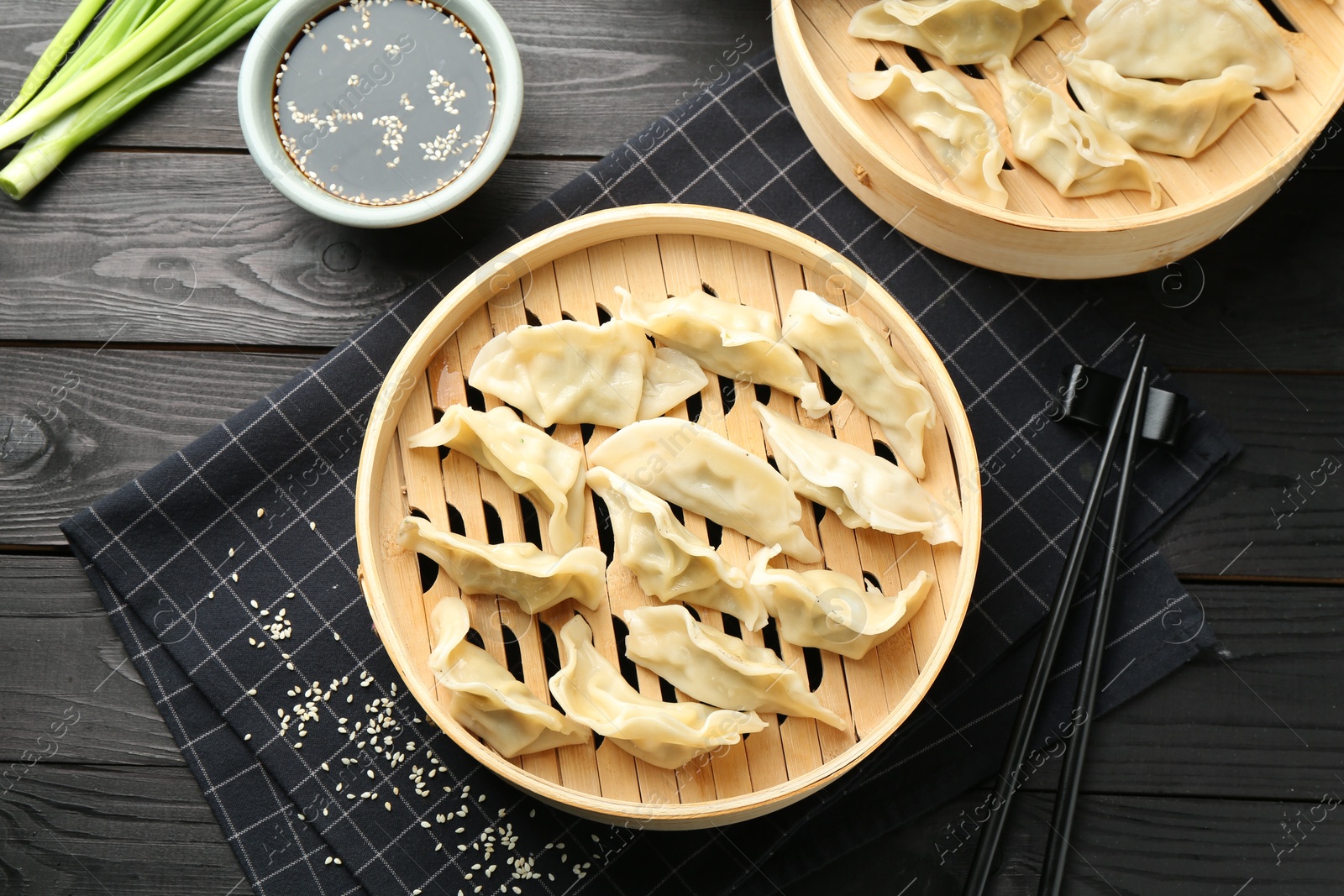 Photo of Tasty boiled gyoza (dumplings) served on black wooden table, flat lay