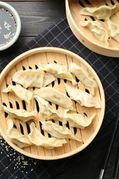 Photo of Tasty boiled gyoza (dumplings) served on black wooden table, flat lay