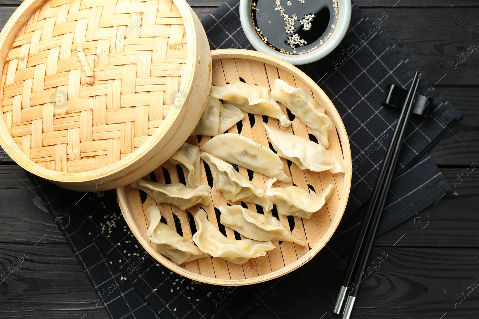 Photo of Tasty boiled gyoza (dumplings) served on black wooden table, flat lay