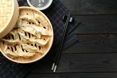 Photo of Tasty boiled gyoza (dumplings) served on black wooden table, flat lay. Space for text