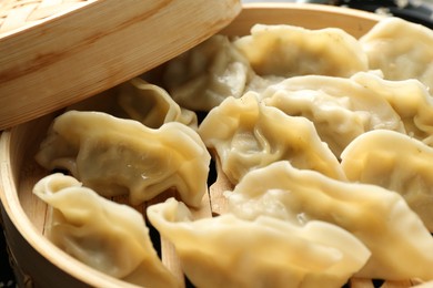 Photo of Tasty boiled gyoza (dumplings) in bamboo steamer on table, closeup