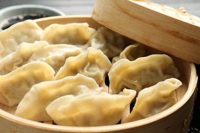 Photo of Tasty boiled gyoza (dumplings) in bamboo steamer on table, closeup