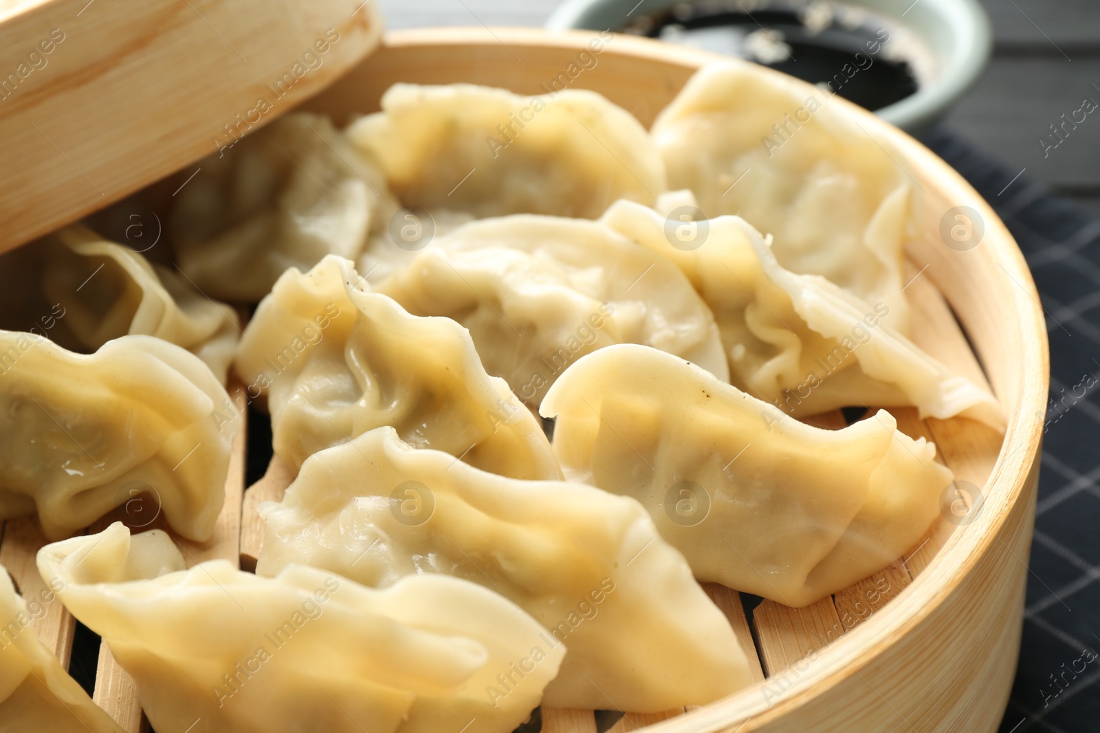 Photo of Tasty boiled gyoza (dumplings) in bamboo steamer on table, closeup