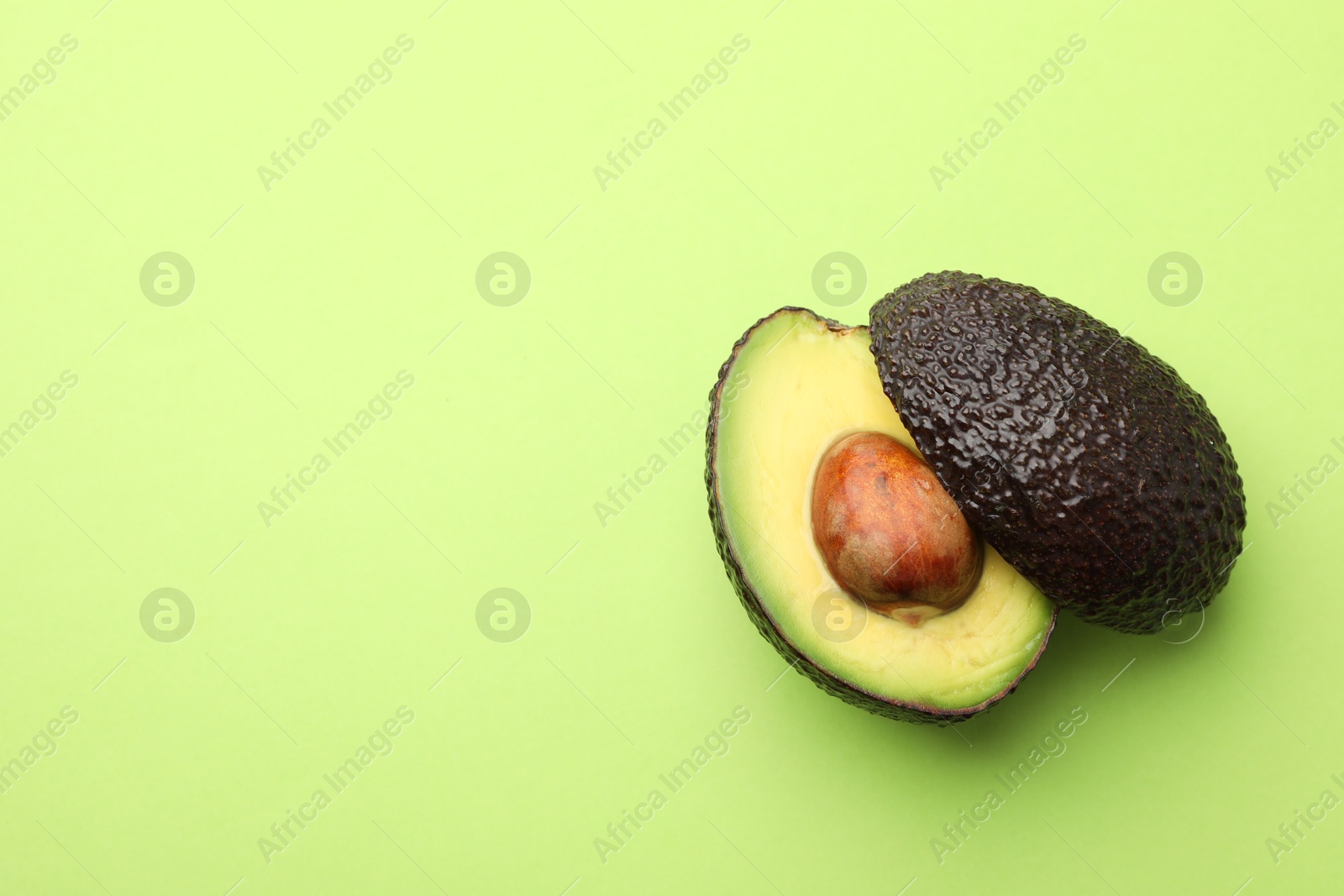 Photo of One cut ripe avocado on light green background, top view. Space for text