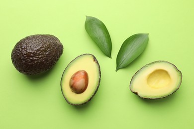 Photo of Fresh ripe avocados and leaves on light green background, flat lay