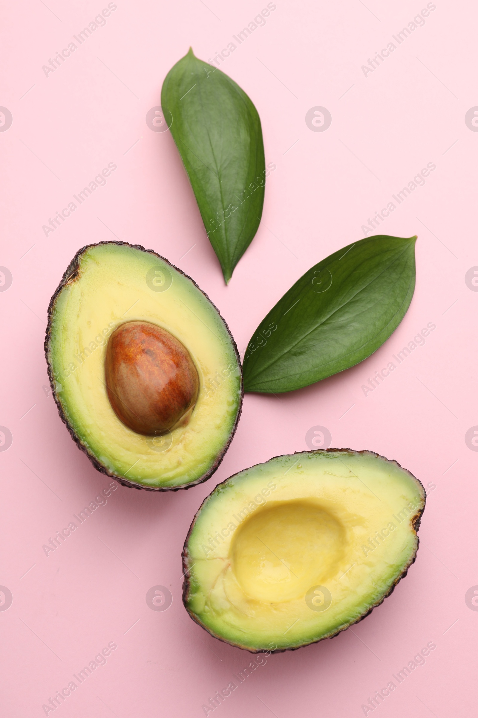 Photo of One cut ripe avocado and leaves on pink background, flat lay