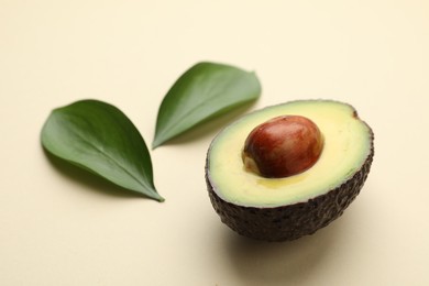 Photo of One cut ripe avocado and leaves on beige background, closeup