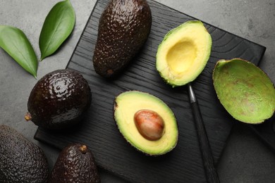 Photo of Fresh ripe avocados, spoon and leaves on grey table, flat lay