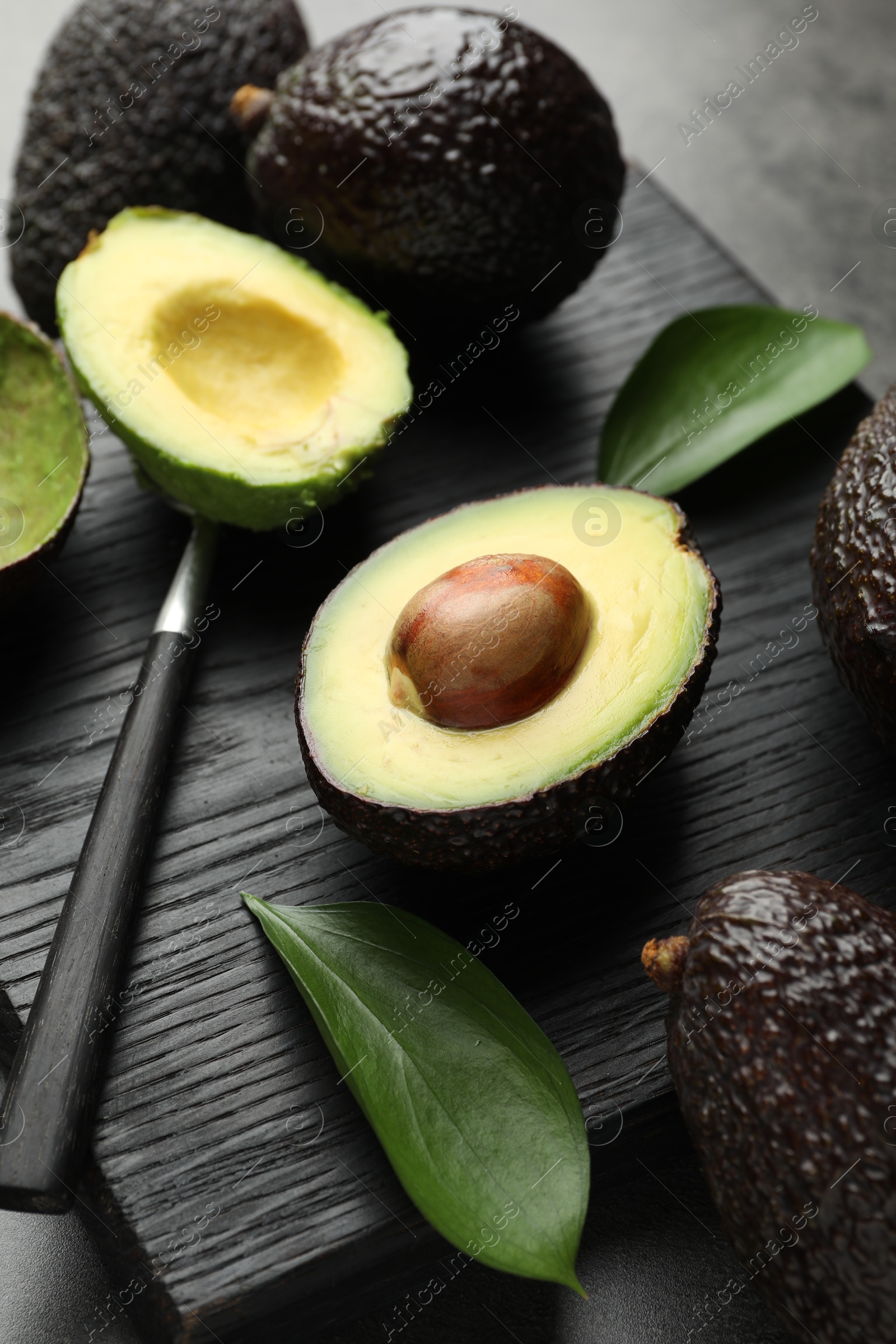 Photo of Fresh ripe avocados, spoon and leaves on grey table, closeup