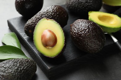 Photo of Fresh ripe avocados, spoon and leaves on grey table, closeup