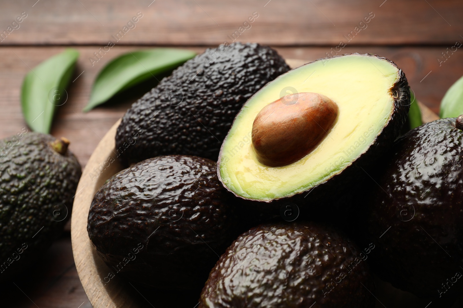 Photo of Fresh ripe avocados and leaves on wooden table, closeup