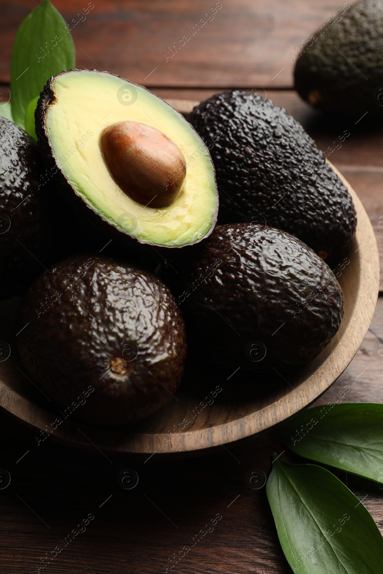 Photo of Fresh ripe avocados and leaves on wooden table, closeup