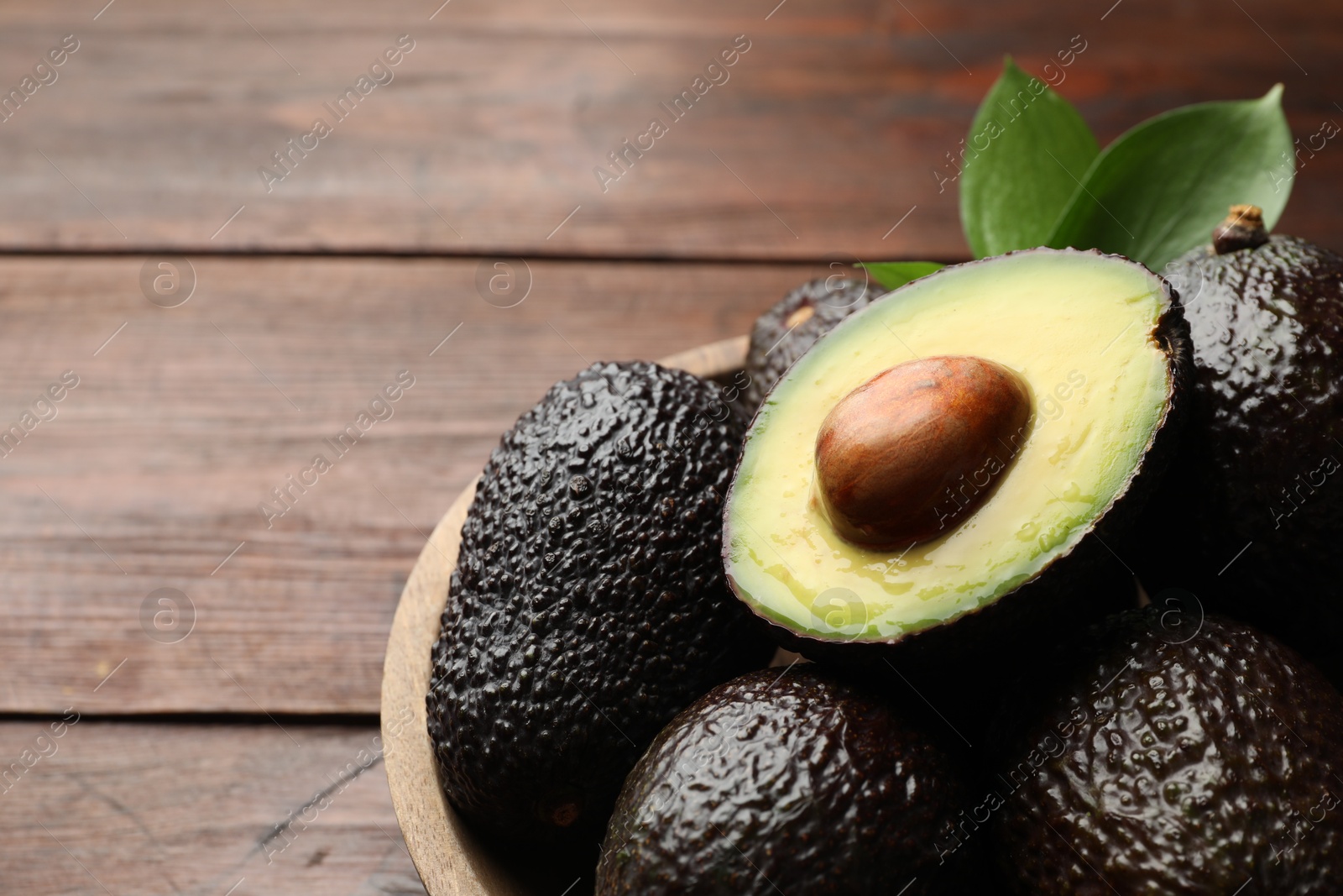 Photo of Fresh ripe avocados and leaves on wooden table, closeup. Space for text