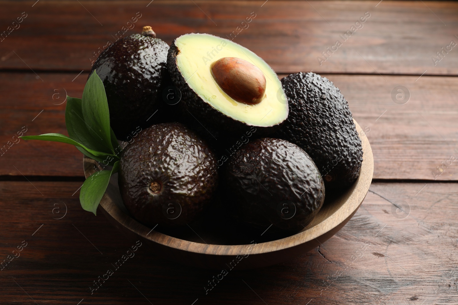 Photo of Fresh ripe avocados and leaves on wooden table, closeup