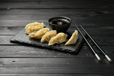 Photo of Tasty boiled gyoza (dumplings) served on black wooden table