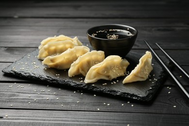 Photo of Tasty boiled gyoza (dumplings) served on black wooden table, closeup