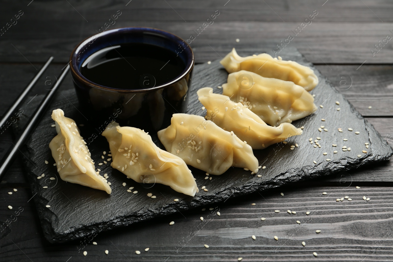 Photo of Tasty boiled gyoza (dumplings) served on black wooden table, closeup