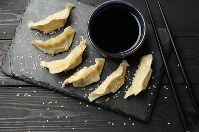 Photo of Tasty boiled gyoza (dumplings) served on black wooden table, flat lay