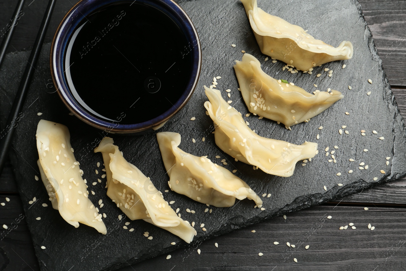 Photo of Tasty boiled gyoza (dumplings) served on black wooden table, flat lay