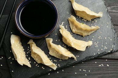 Photo of Tasty boiled gyoza (dumplings) served on black wooden table, flat lay