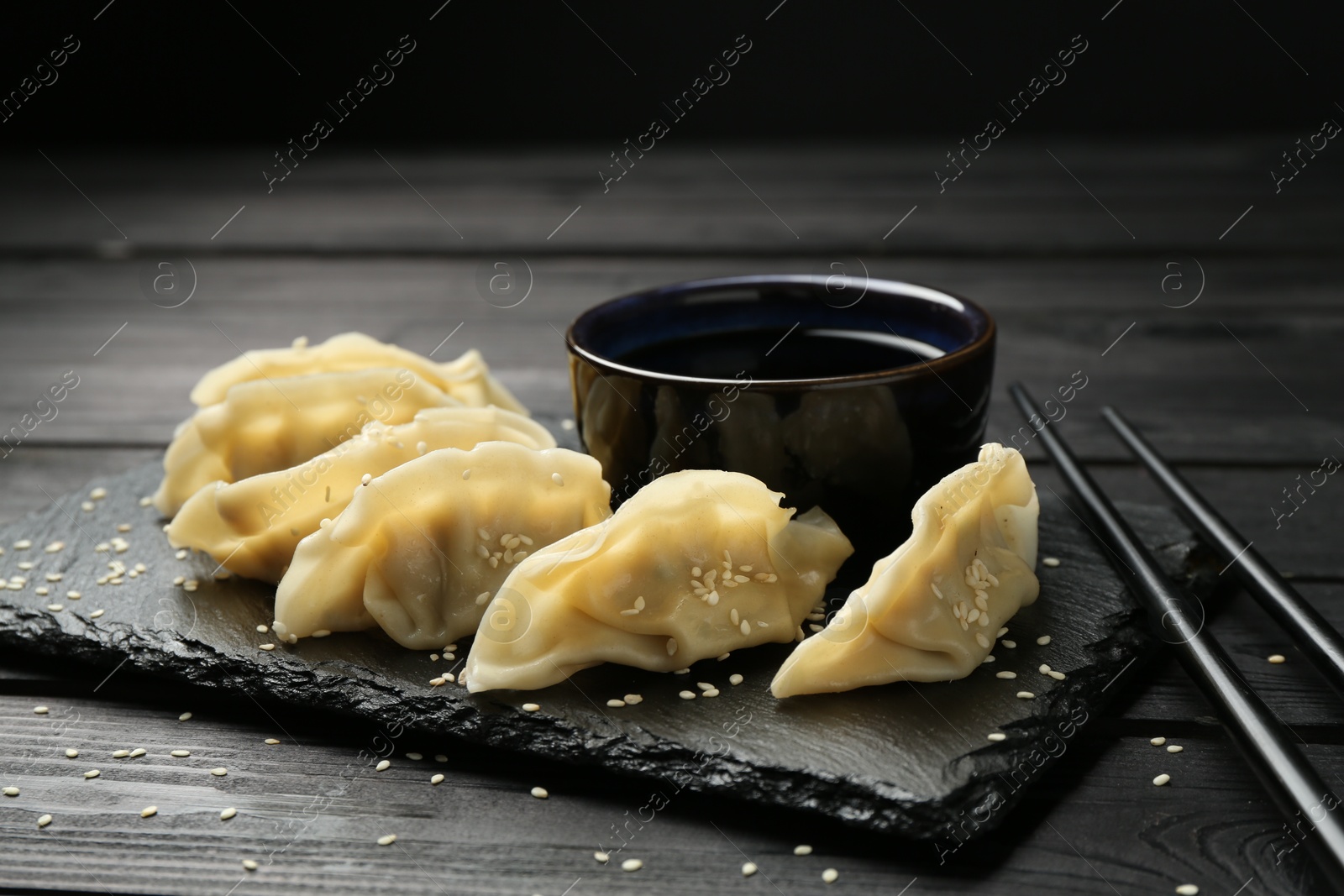 Photo of Tasty boiled gyoza (dumplings) served on black wooden table, closeup