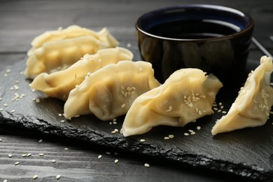 Photo of Tasty boiled gyoza (dumplings) with soy sauce and sesame on black wooden table, closeup