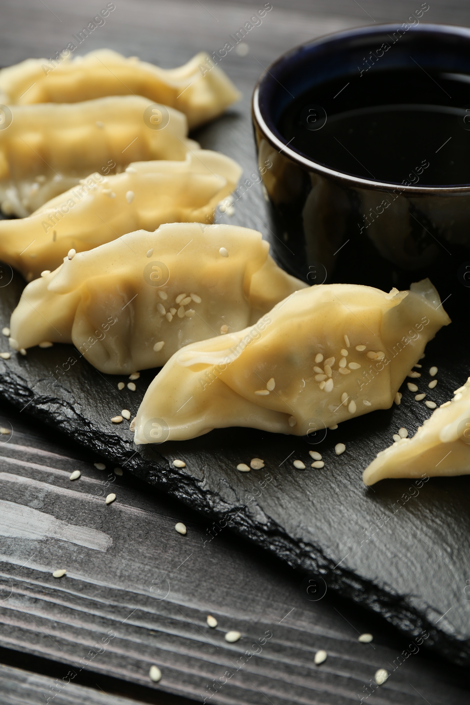 Photo of Tasty boiled gyoza (dumplings) with soy sauce and sesame on black wooden table, closeup