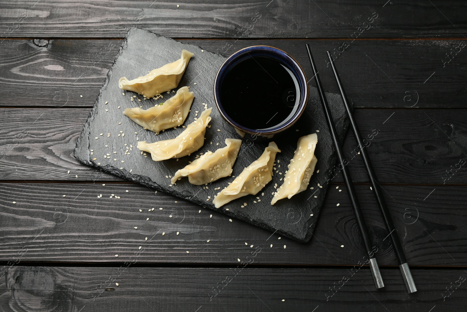 Photo of Tasty boiled gyoza (dumplings) served on black wooden table, flat lay