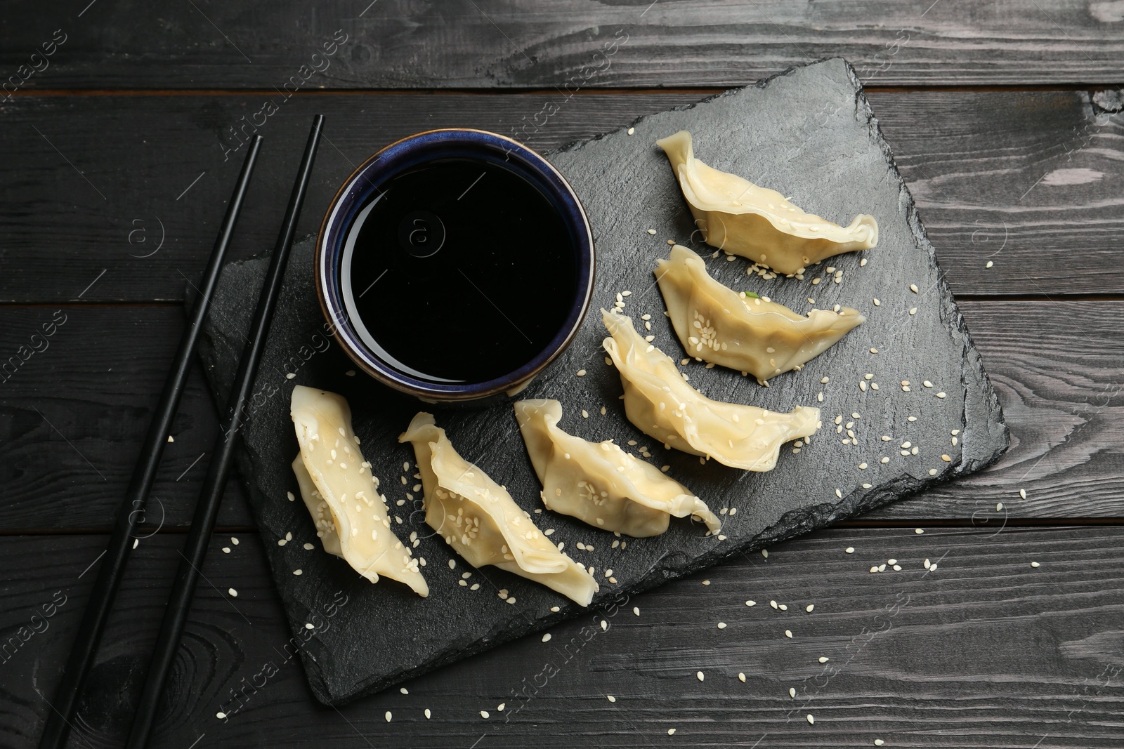 Photo of Tasty boiled gyoza (dumplings) served on black wooden table, flat lay