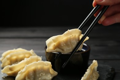 Photo of Woman taking tasty gyoza (dumpling) with chopsticks at black table, closeup