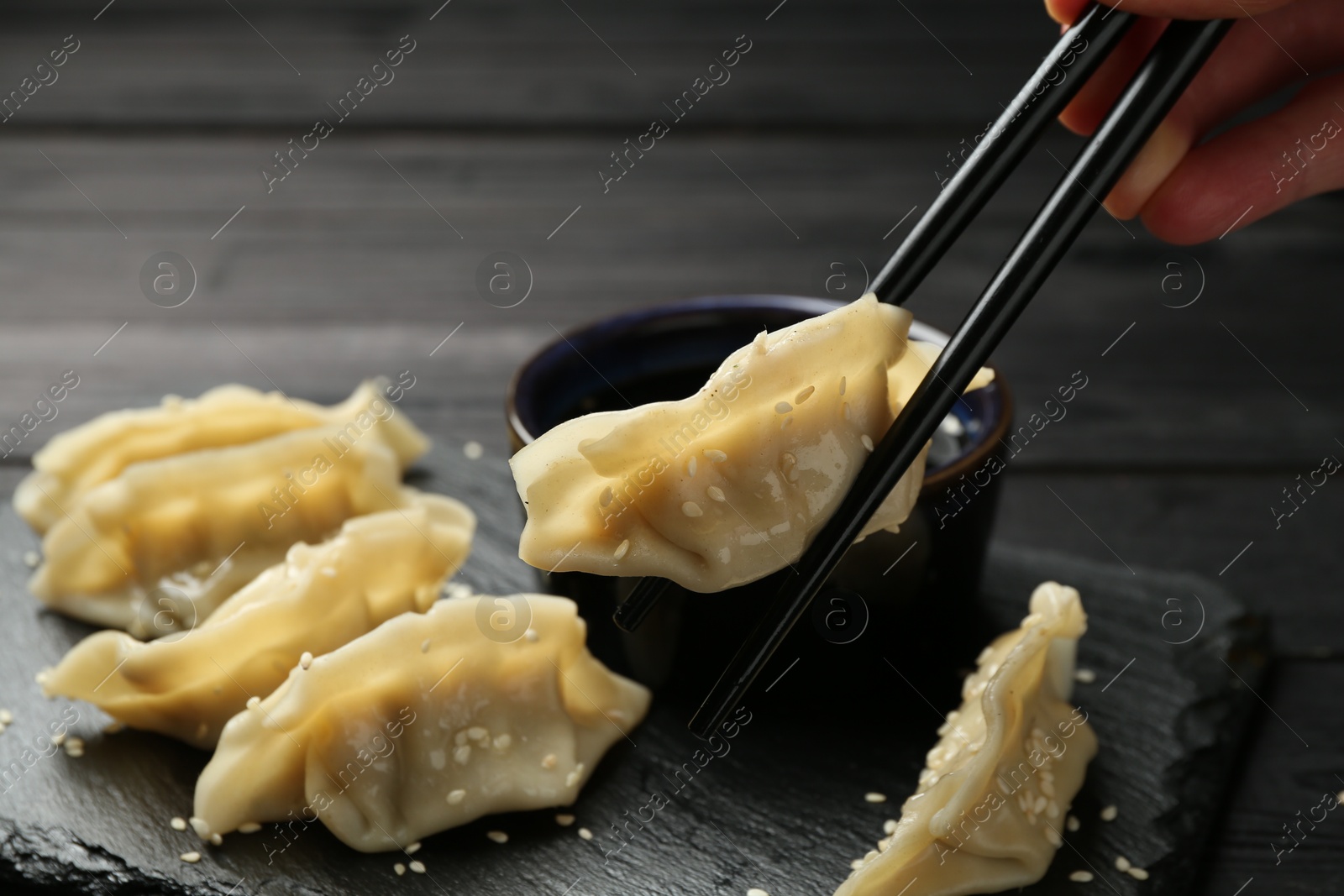 Photo of Woman taking tasty gyoza (dumpling) with chopsticks at black table, closeup