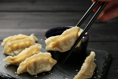 Photo of Woman taking tasty gyoza (dumpling) with chopsticks at black table, closeup