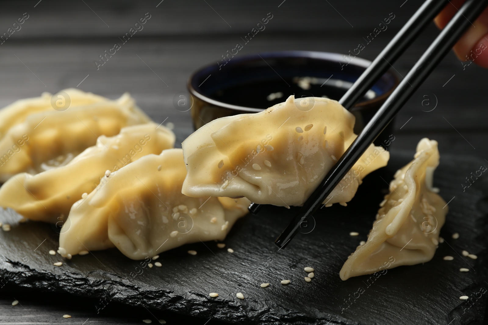 Photo of Woman taking tasty gyoza (dumpling) with chopsticks at black table, closeup