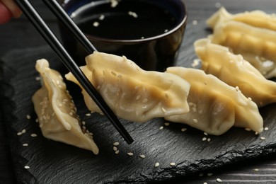 Photo of Taking tasty gyoza (dumpling) with chopsticks at black table, closeup