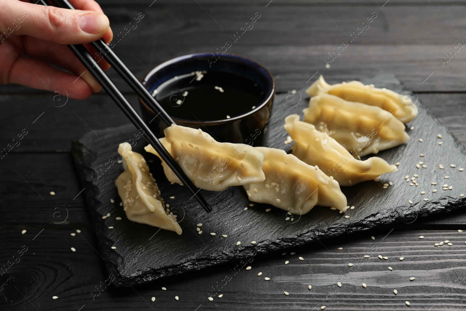 Photo of Woman taking tasty gyoza (dumpling) with chopsticks at black wooden table, closeup