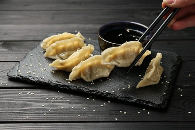 Photo of Woman taking tasty gyoza (dumpling) with chopsticks at black wooden table, closeup